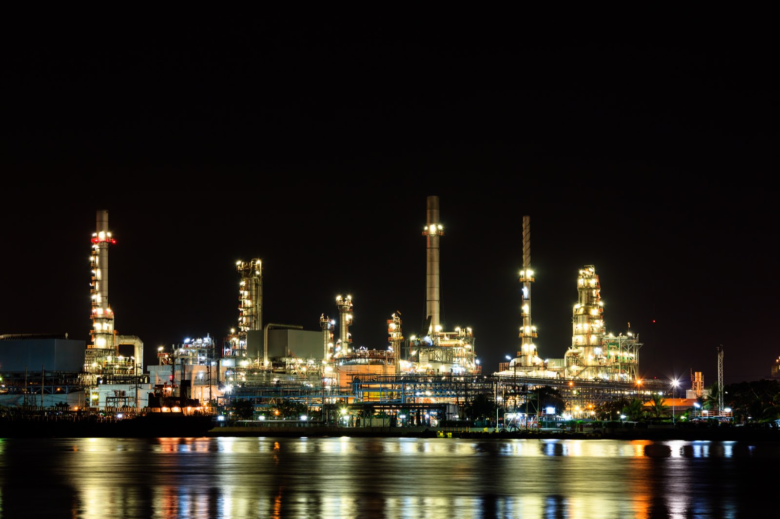 Refinery lit at night, reflected in the water alongside it